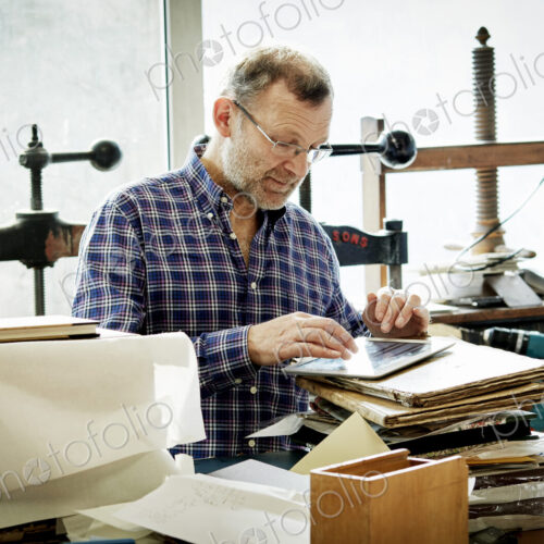 A man using a digital tablet in a bookbinding workshop.