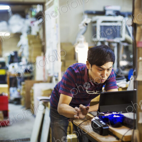 A man using a laptop computer, working in a glass maker's workshop. A man using a laptop computer, working in a glass maker's workshop.