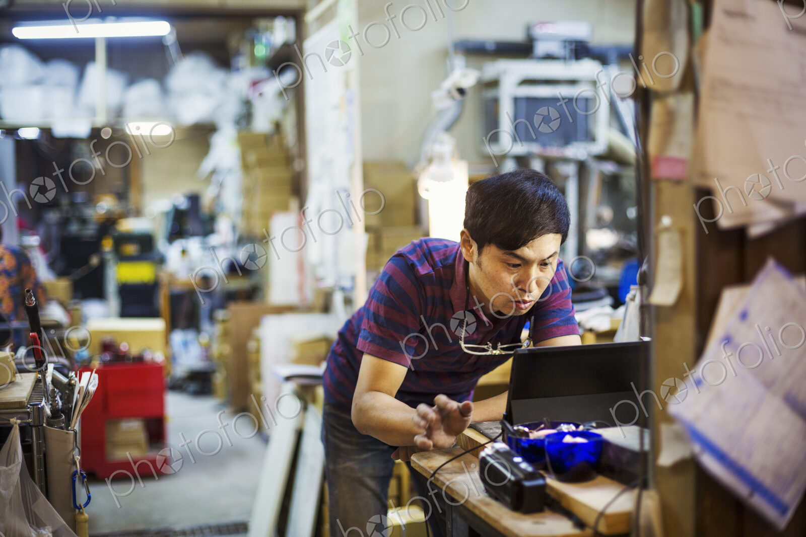 A man using a laptop computer, working in a glass maker’s workshop.