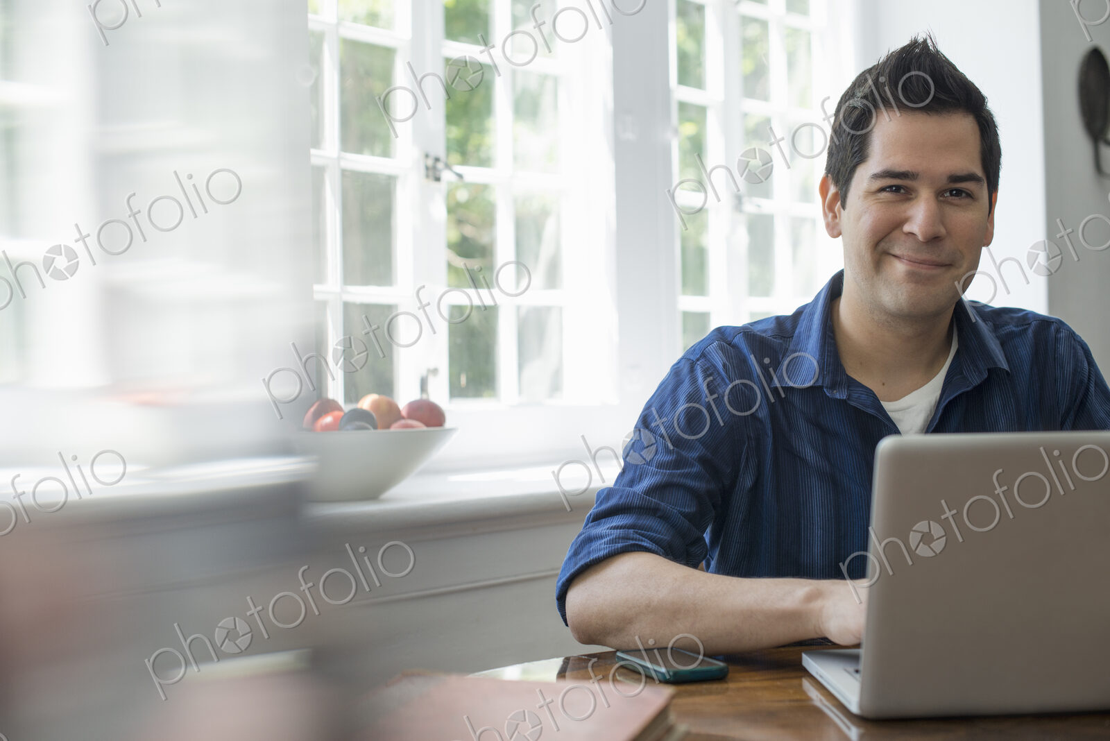 A man using a laptop seated at a table by a window. Working from home.