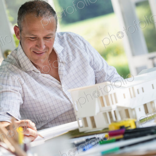 A man using a pencil drawing on a plan using an architectural model A man using a pencil drawing on a plan using an architectural model