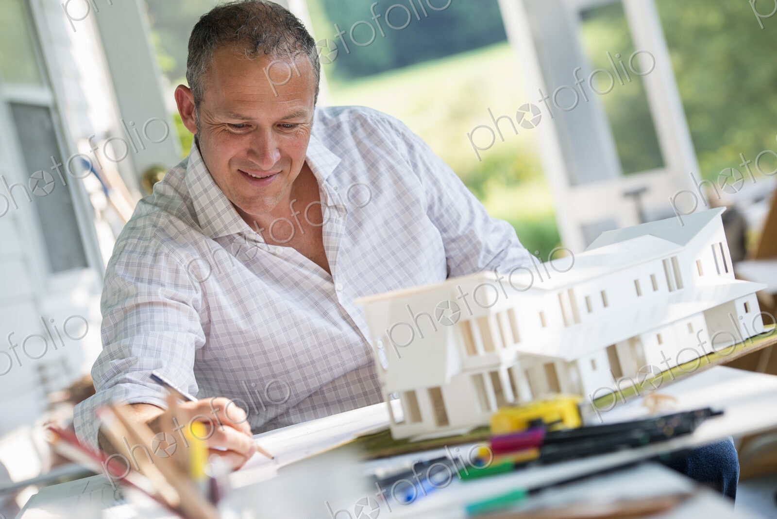 A man using a pencil drawing on a plan using an architectural model
