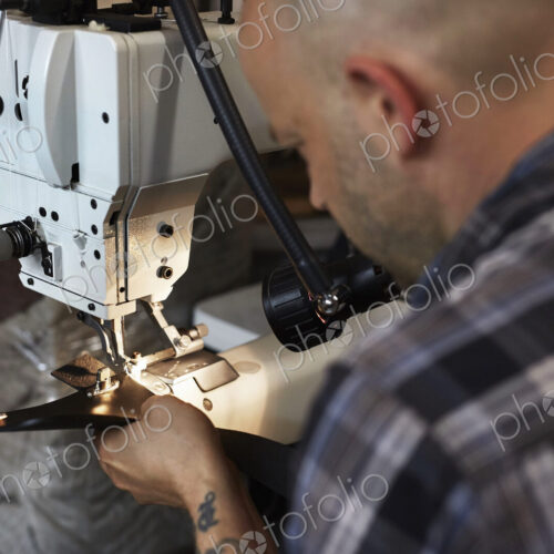A man using an industriall sewing machine, stitching leather handmade goods.