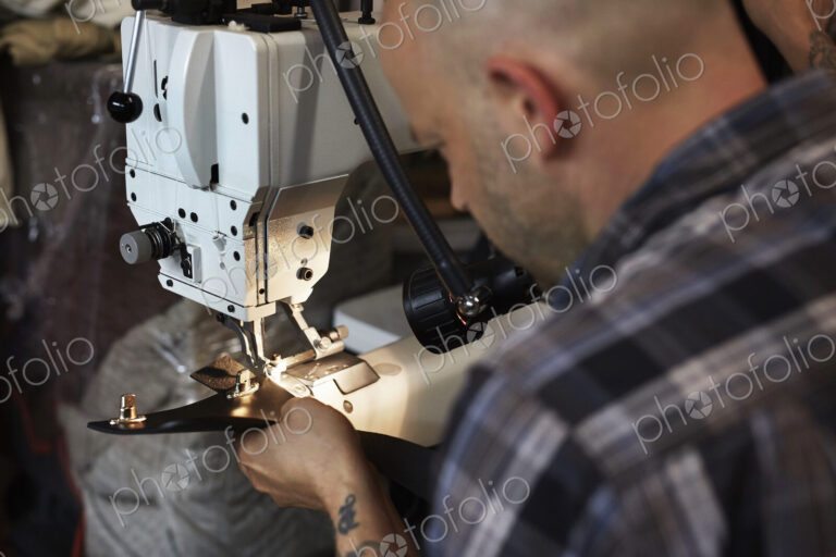 A man using an industriall sewing machine, stitching leather handmade goods.