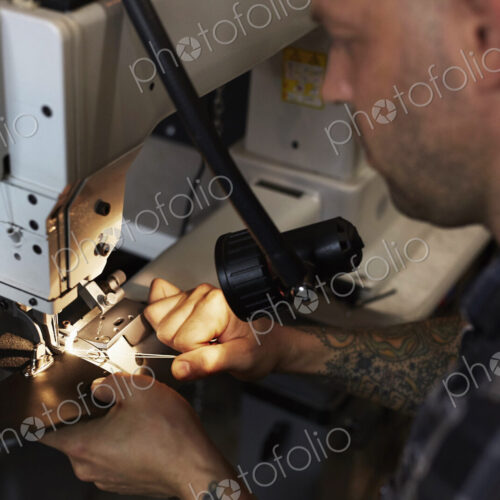 A man using an industriall sewing machine, stitching leather handmade goods.