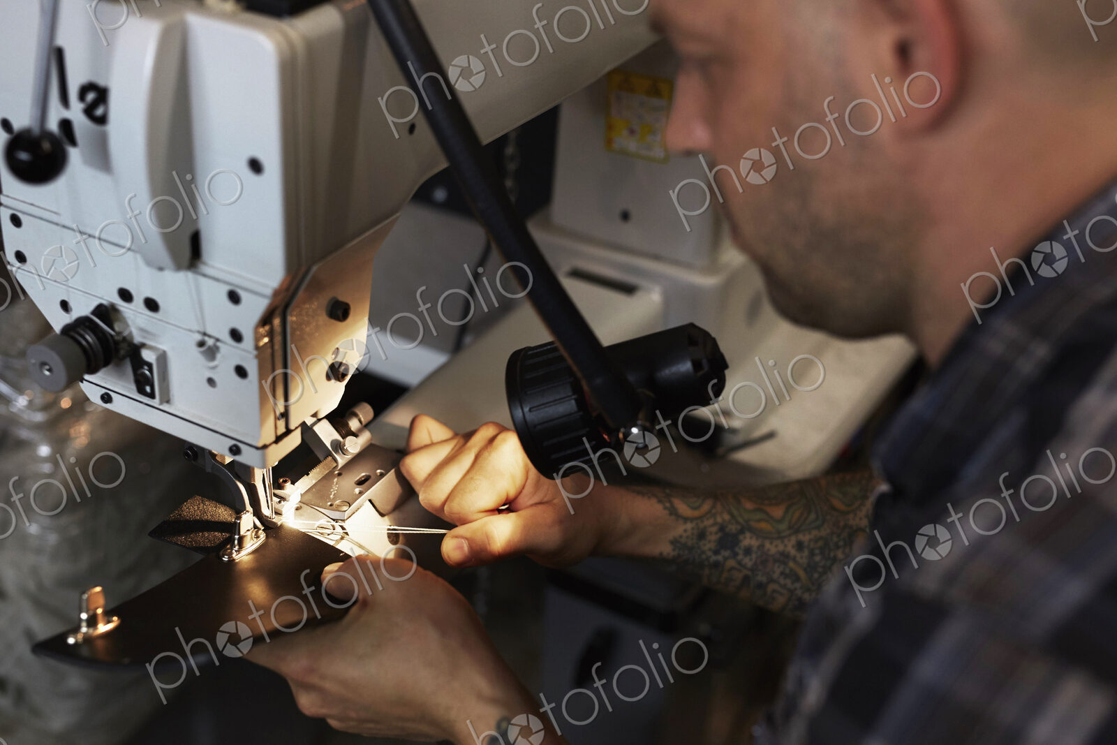 A man using an industrial sewing machine, stitching leather handmade goods.