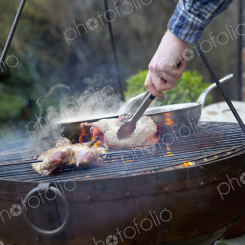 A man using tongs to move roasting game bird pieces on a barbeque. A man using tongs to move roasting game bird pieces on a barbeque.
