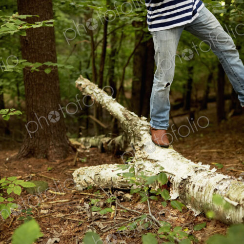 A man walking along a fallen tree trunk in the woods, balancing with one leg raised in…
