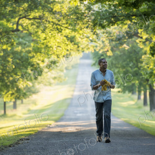 A man walking down a tree lined avenue in the countryside.