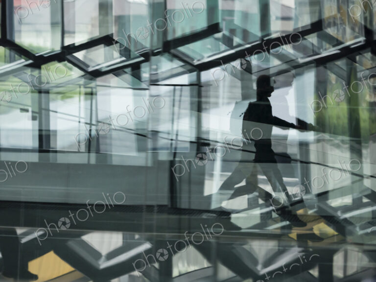 A man walking through the Harpa building, with glass walls and reflected light.