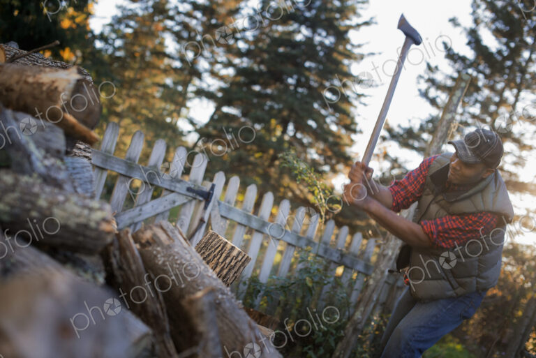 A man wielding an axe, and chopping wood, splitting logs for the fire.