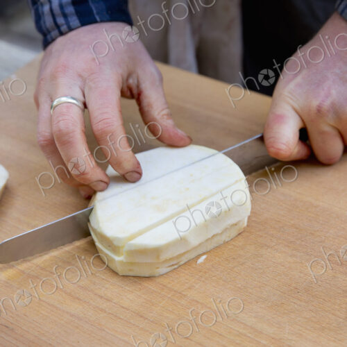 A man with a long knife chopping celeriac into cubes on a chopping board.