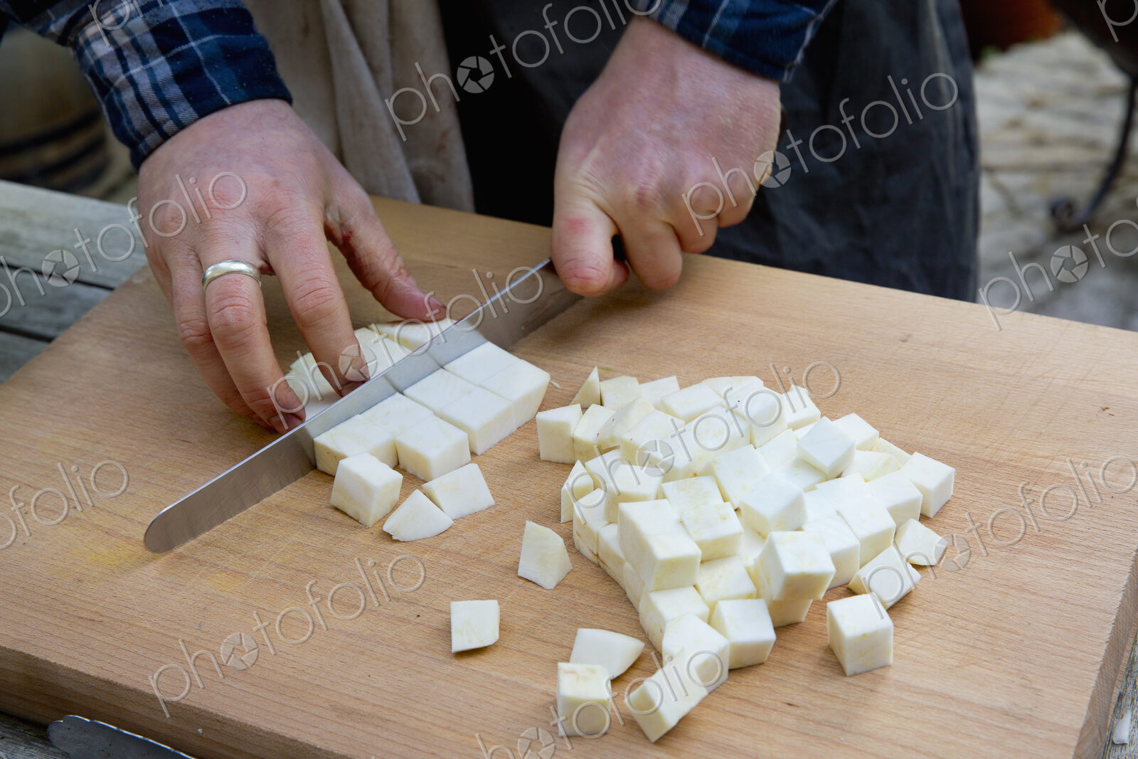 A man with a long knife chopping celeriac into cubes on a chopping board.