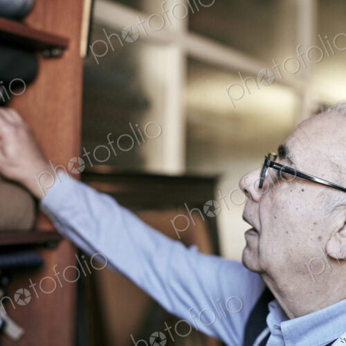 A man with grey hair and glasses reaching up to select fabrics from the choice of cloth. A man with grey hair and glasses reaching up to select fabrics from the choice of cloth.