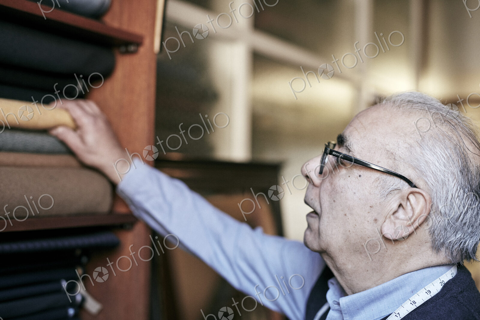 A man with grey hair and glasses reaching up to select fabrics from the choice of cloth.