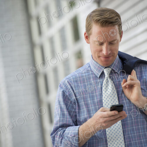 A man with his jacket slung over his shoulder, checking his phone. A man with his jacket slung over his shoulder, checking his phone.