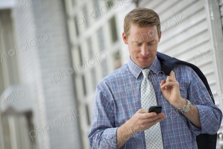 A man with his jacket slung over his shoulder, checking his phone.