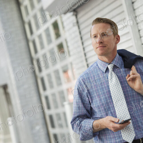 A man with his jacket slung over his shoulder, checking his phone. A man with his jacket slung over his shoulder, checking his phone.