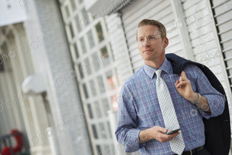 A man with his jacket slung over his shoulder, checking his phone.