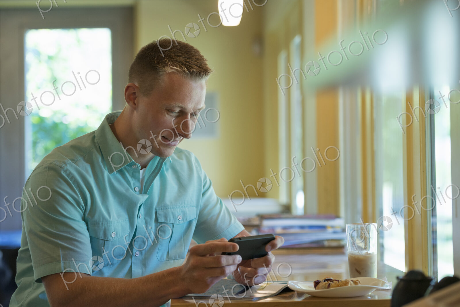 A man with short cropped hair sitting at a cafe table, using a smart phone.