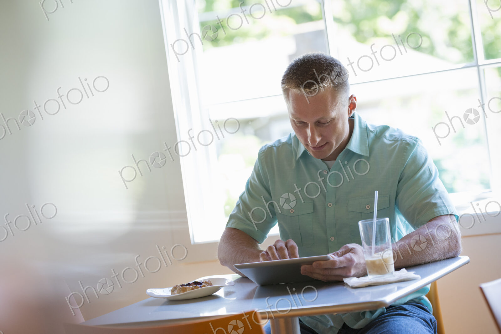 A man with short cropped hair sitting at a cafe table. Using a digital tablet.