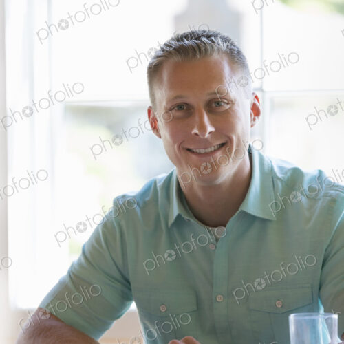 A man with short cropped hair sitting at a cafe table. Using a digital tablet.