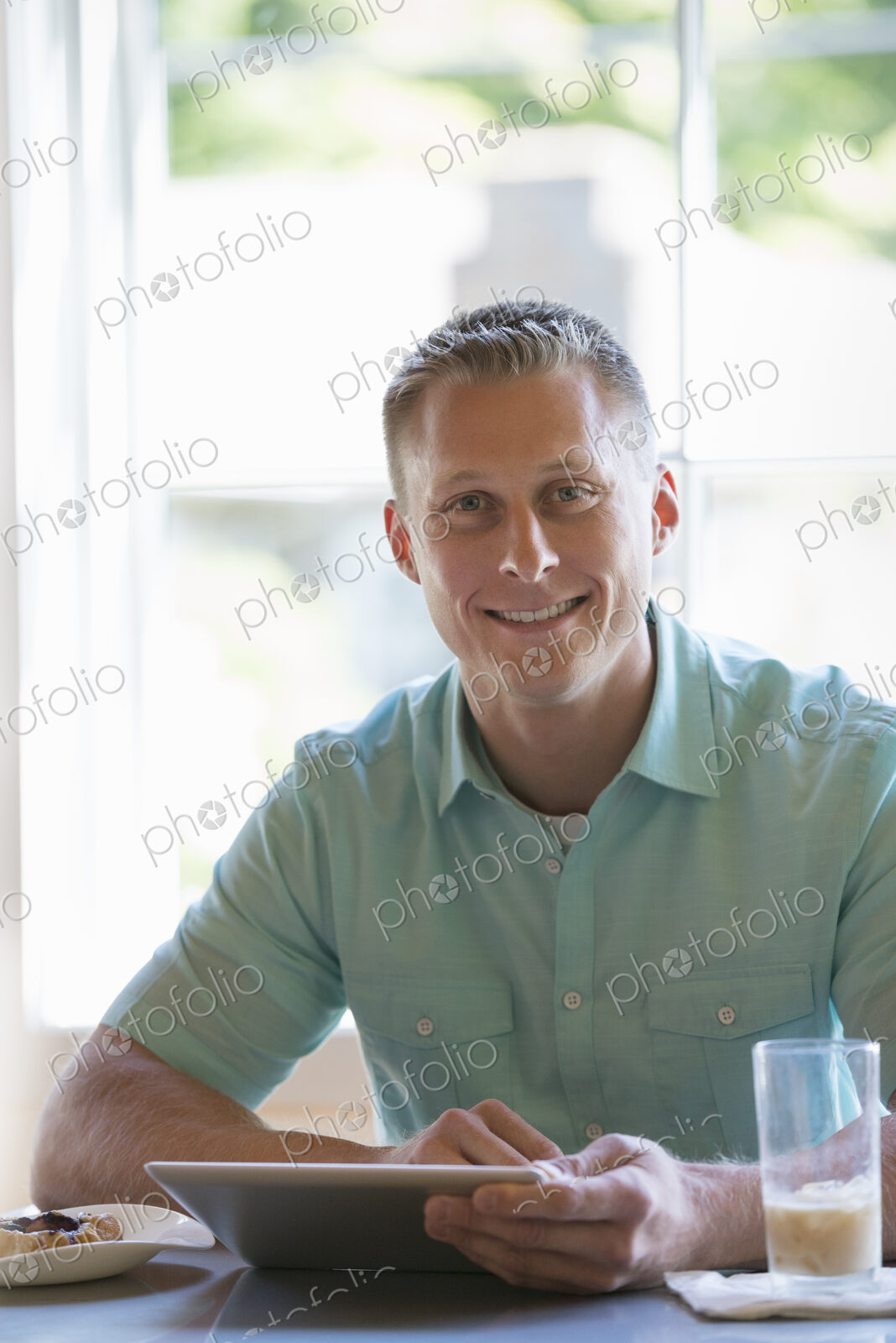 A man with short cropped hair sitting at a cafe table. Using a digital tablet.