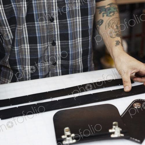 A man with tattoed arms, craftsman working at a bench, smoothing strips of tanned… A man with tattoed arms, craftsman working at a bench, smoothing strips of tanned…