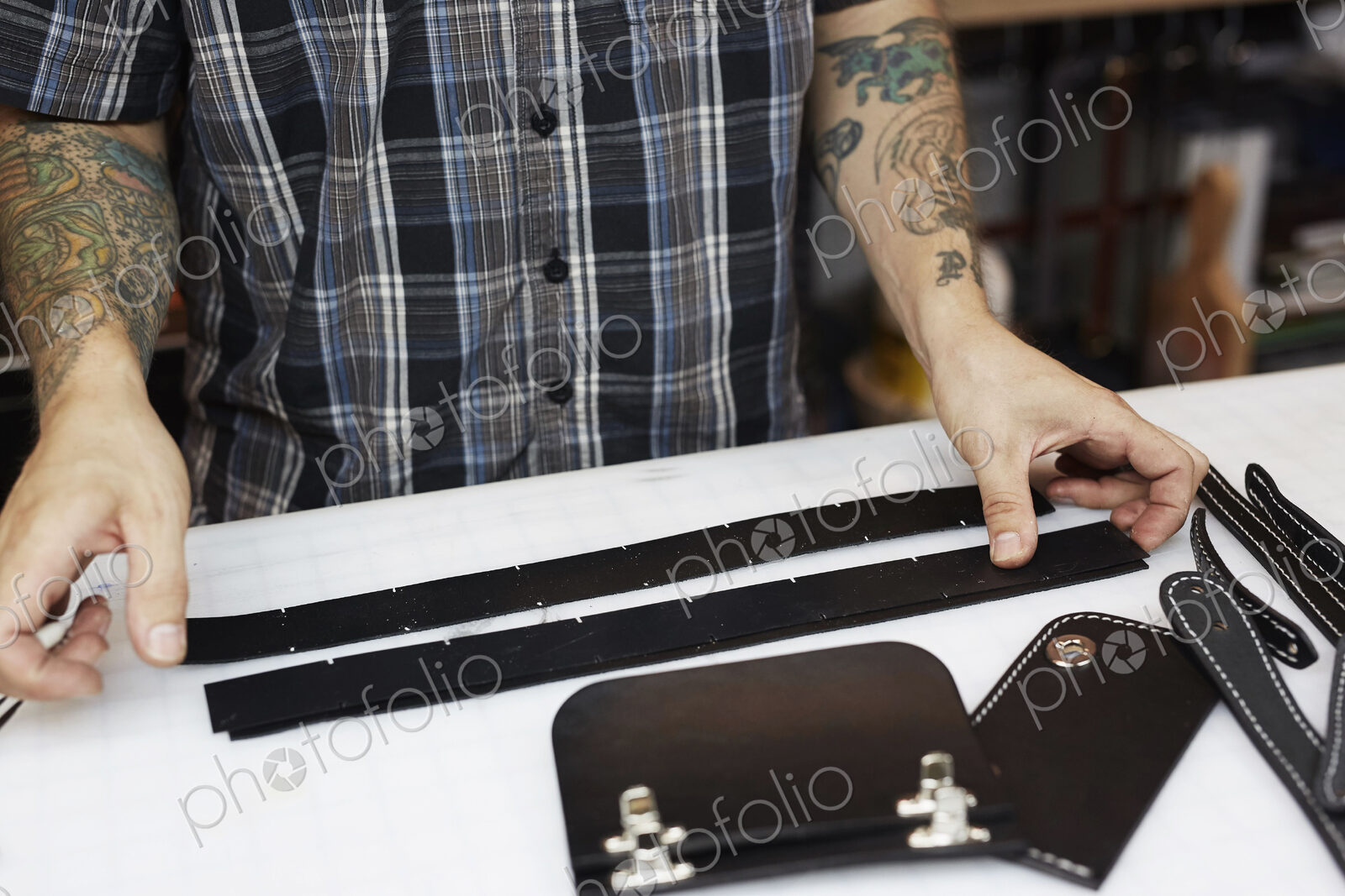 A man with tattoed arms, craftsman working at a bench, smoothing strips of tanned…