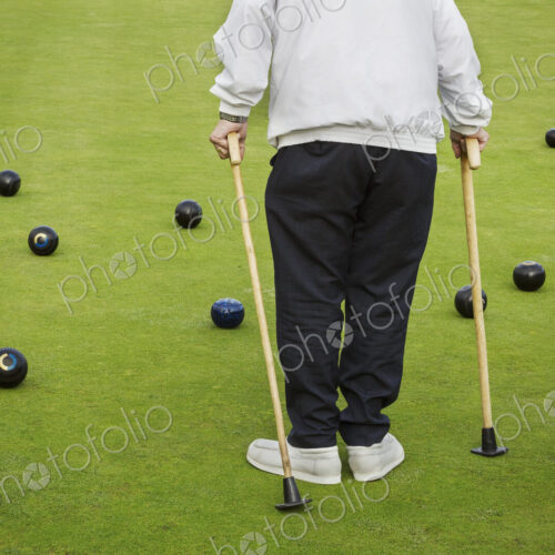 A man with two walking sticks standing on a lawn bowls green, with bowls balls… A man with two walking sticks standing on a lawn bowls green, with bowls balls…