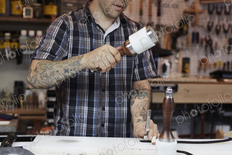 A man working at a bench in a leather workshop, using a mallet and chisel to mark leather.