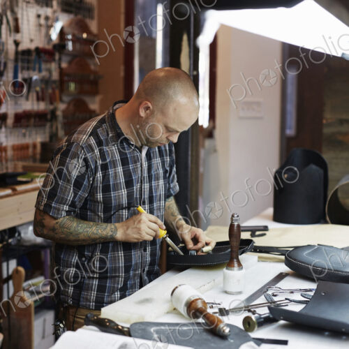 A man working at a bench under a bright light in a leather workshop. A large tool… A man working at a bench under a bright light in a leather workshop. A large tool…