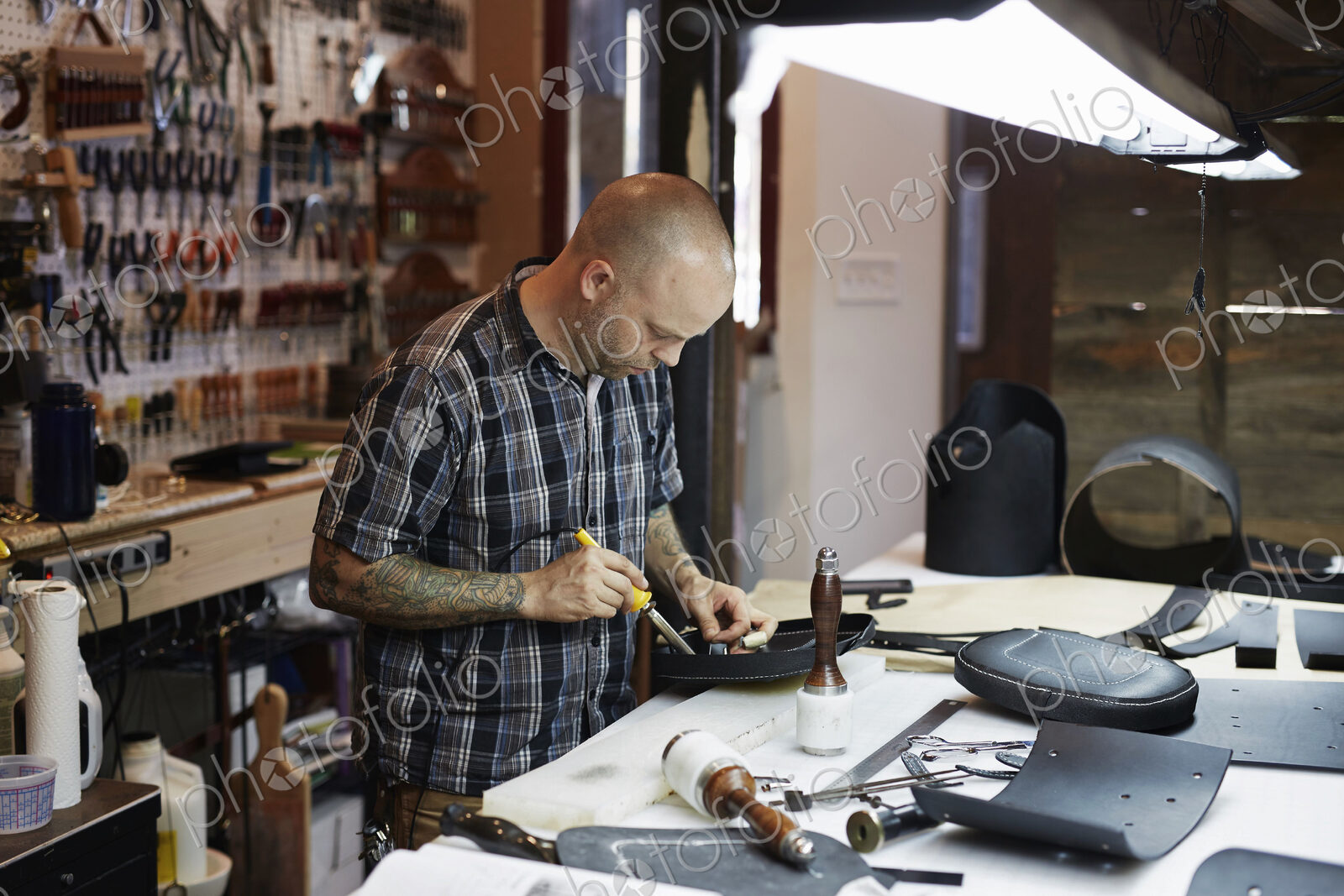 A man working at a bench under a bright light in a leather workshop. A large tool…