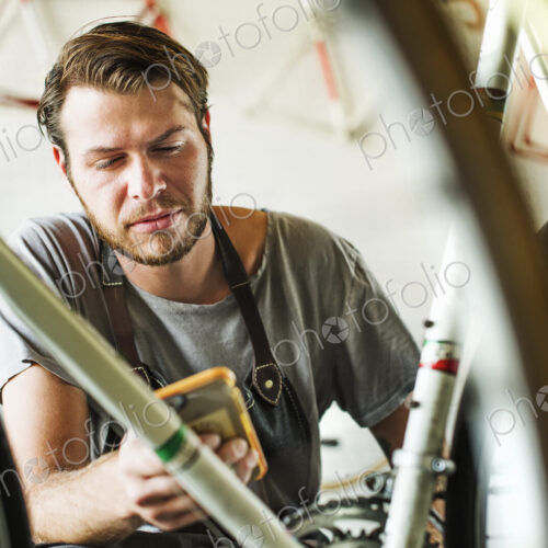 A man working in a bicycle repair shop, checking his smart phone. A man working in a bicycle repair shop, checking his smart phone.