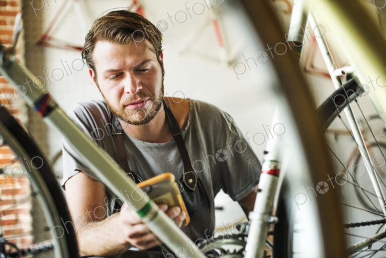 A man working in a bicycle repair shop, checking his smart phone.