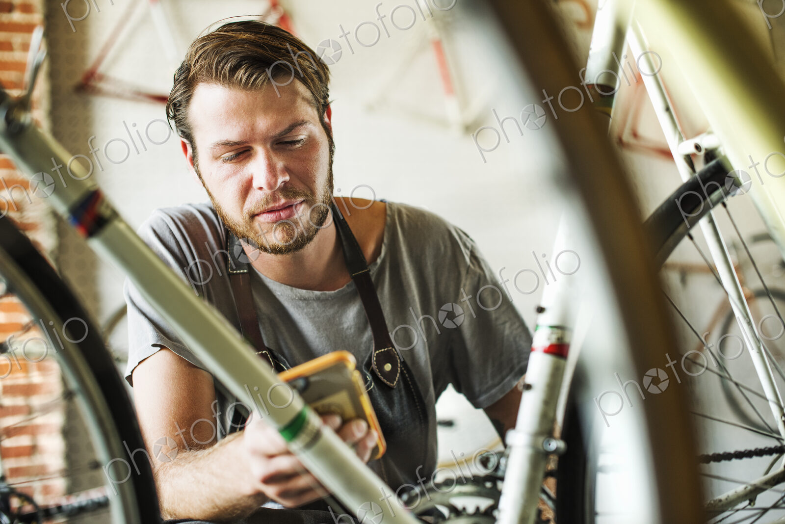 A man working in a bicycle repair shop, checking his smart phone.