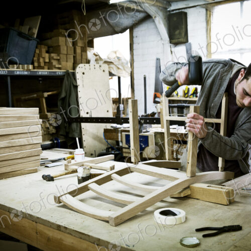 A man working in a furniture maker's workshop assembling a chair.