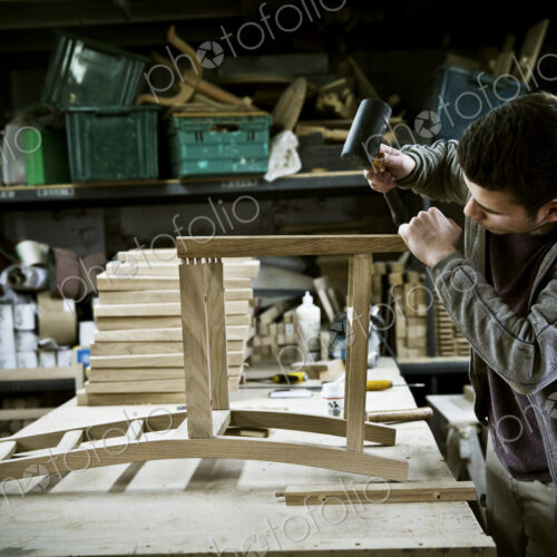 A man working in a furniture maker's workshop assembling a chair. A man working in a furniture maker's workshop assembling a chair.
