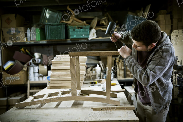 A man working in a furniture maker's workshop assembling a chair.