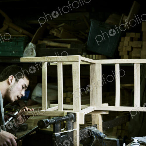 A man working in a furniture maker's workshop assembling a chair. A man working in a furniture maker's workshop assembling a chair.