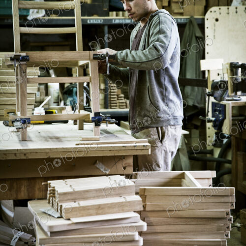 A man working in a furniture maker's workshop assembling a chair.