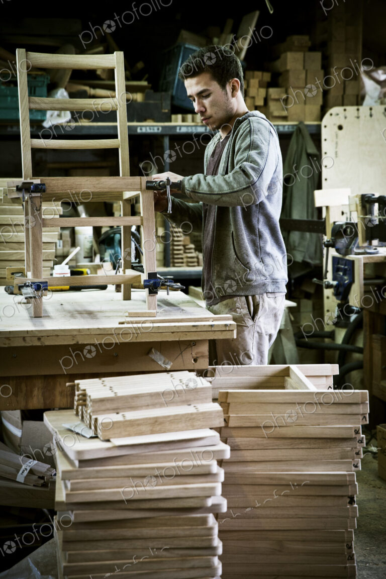 A man working in a furniture maker's workshop assembling a chair.