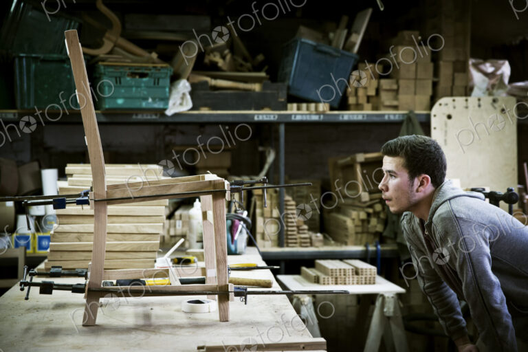 A man working in a furniture maker's workshop assembling a chair.