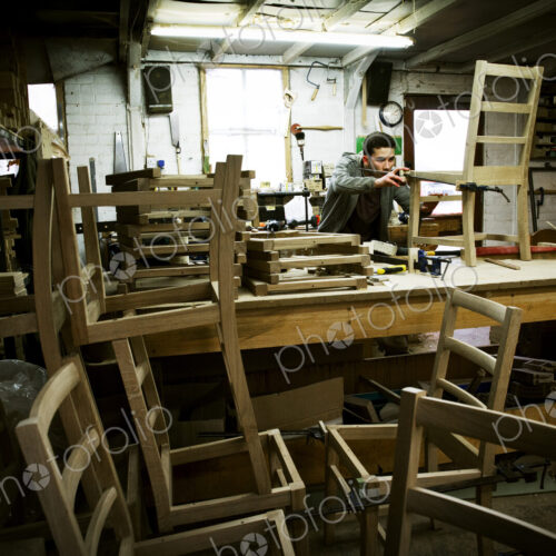 A man working in a furniture maker's workshop assembling a chair. A man working in a furniture maker's workshop assembling a chair.