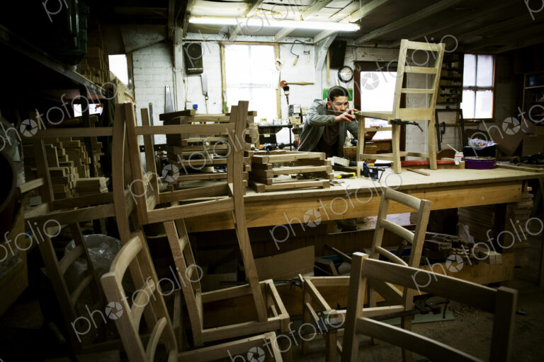 A man working in a furniture maker's workshop assembling a chair.