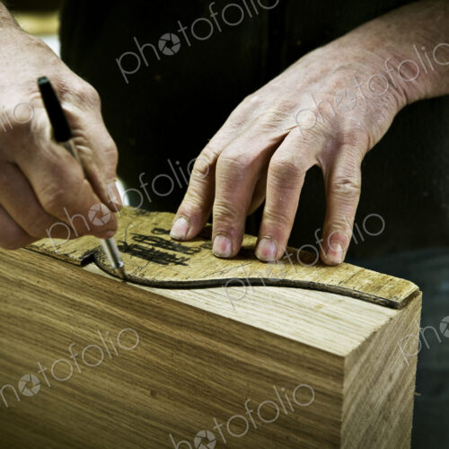 A man working in a furniture maker's workshop drawing around a shape on wood. A man working in a furniture maker's workshop drawing around a shape on wood.