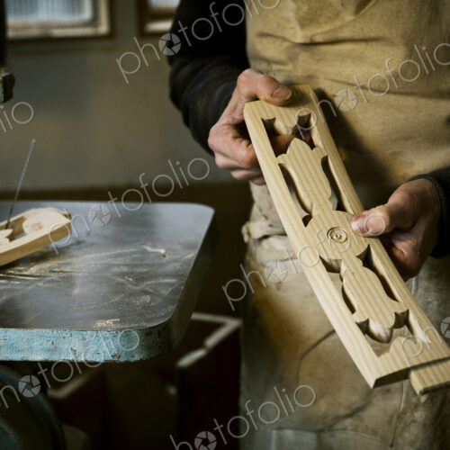 A man working in a furniture maker's workshop holding shaped carved chair back struts.