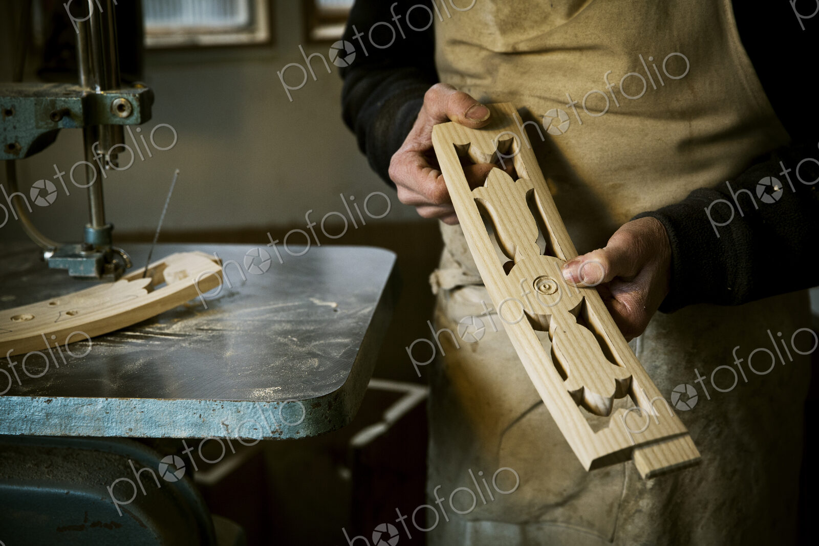 A man working in a furniture maker’s workshop holding shaped carved chair back struts.