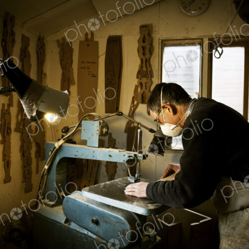 A man working in a furniture maker's workshop, using a machine saw. A man working in a furniture maker's workshop, using a machine saw.