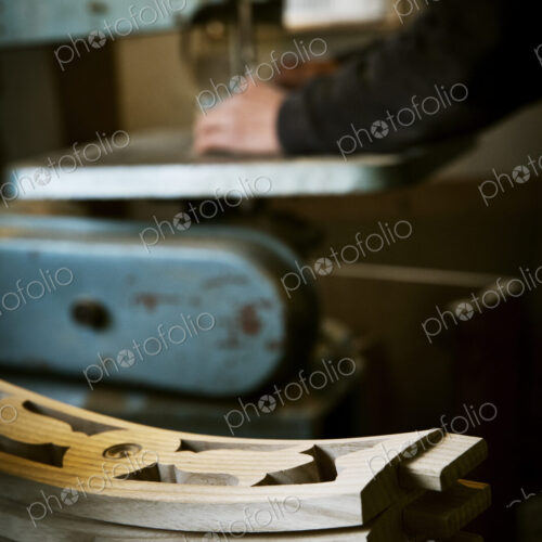 A man working in a furniture maker's workshop using a mechanical saw. Wooden chair…